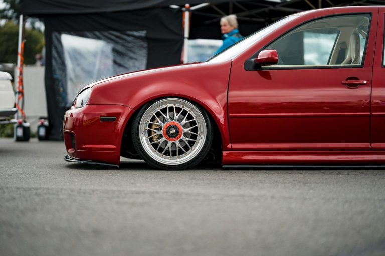 ceramic coated Low-profile red car with white wheels, parked on asphalt at an event.